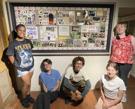 Five students standing and seated around a bulletin board